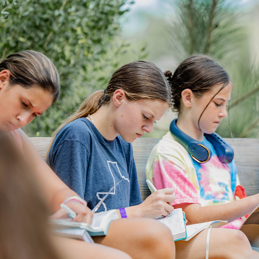 Campers reading and journaling in their Bibles together outdoors at Camp Cho-Yeh