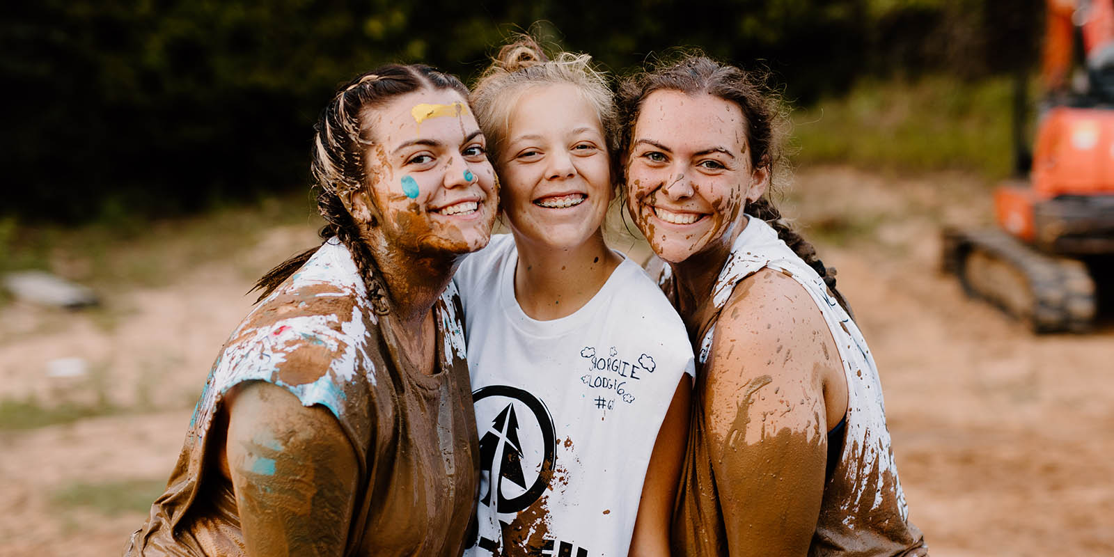 Three Camp Cho-Yeh campers covered in mud, arms around each other, laughing